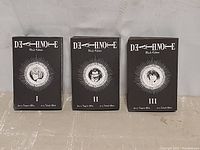 Three hardcover Death Note Black Edition books showing front covers with character illustrations and volume numbering I, II, III.