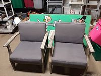 Photo showing two wooden framed outdoor patio chairs with gray cushions in a storage area, some wear visible on arms.