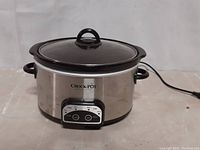 Front view of small Crock-Pot with stainless steel body, glass lid, and control panel showing low, high, and warm buttons.