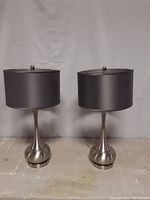 Two brushed nickel table lamps with matte black drum shades, shown side by side against a plain background.