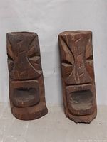 Two totems side by side, showing carved faces and overall shape, highlighting the rustic wood texture.