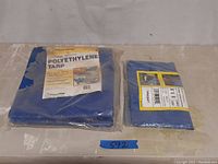 Two polyethylene tarps folded and in original plastic packaging, one significantly larger than the other, both blue in color.