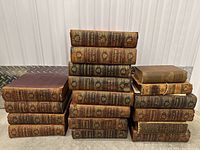 Stack of antique leather-bound books showing spines with volume numbers and titles such as Encyclopaedia Britannica and others, many volumes in worn condition