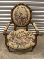 Full view of antique wooden armchair showing floral needlepoint upholstery and carved wooden frame.