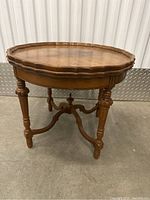 Full view of the antique wooden side table showing scalloped edge top and tripod leg base with stretcher.