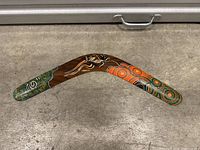 Decorated Aboriginal-style wooden boomerang with dot painting and patterns in green, brown, white, orange, and black colors.