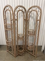 Full view of folding rattan brown plant stand with three arched panels and circular holders for plants.