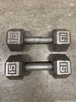 Pair of hexagonal 15 lb dumbbells with metal handles and some wear marks, laying on a concrete floor.