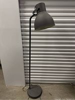 Full view of the IKEA Hector floor lamp showing the entire lamp from base to shade in dark gray metal with power cord.