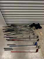 Full view of mixed golf clubs laid out on floor including irons, drivers, putters and head covers