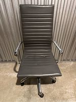 Front view of brown padded office chair with horizontal stitching and chrome armrests and base with wheels