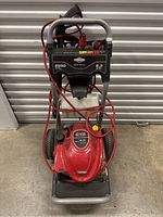 Front view of Briggs & Stratton Elite Series pressure washer, showing full unit with red engine, hose and spray gun.