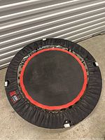 Top-down view of a small circular trampoline showing the black jumping surface with a red ring and the black frame cover.