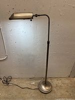 Full view of Verilux floor lamp standing on concrete floor against wall, cord visible.