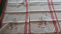 Six vintage linen tea towels laid out showing various embroidered designs including fruits and kitchen items, with red stripes along edges.