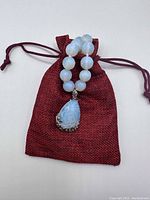 Full moonstone necklace arranged with red woven pouch, showing the bead size and pendant.