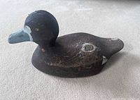 Front and side view of carved wooden duck decoy showing painted head, beak, and body with signs of wear and cracking.