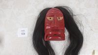 Front view of red-painted carved wooden mask with long dark hair laid flat