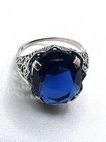 Front view of the ring showing oval deep blue faceted sapphire and decorative filigree silver setting