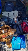 Various bags and two blue Trimark jackets laid out on a surface outdoors.
