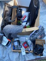 Wide shot of the lot showing black leather briefcase, black Nike backpack, grey neck pillow, packaged tech gadgets and travel items in cardboard boxes.