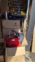 Stack of boxes containing the lot items, including a red bag and black soft-sided bag visible on top.