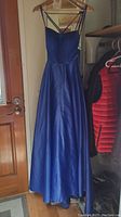 Full-length view of the blue satin evening gown hanging on a wooden hanger showing the skirt and overall length