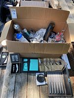 Wide view of box containing bottles and items displayed on wooden surface showing assortment of bottles, accessories and wrapped items.