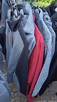Photo showing several jackets and coats hanging on a rack with visible range of colors including grey, red, black.