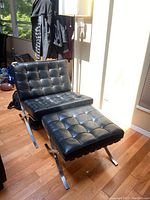 Full view of the black leather chair and ottoman set in a sunlit room with wood flooring.