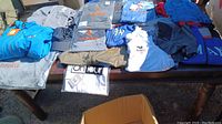 Overview of various jackets and shirts displayed on table, all brand new with tags.