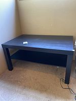 Black rectangular coffee table with lower shelf shown from front angle on carpeted floor.