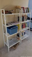 Two white metal shelving units placed side by side filled with various books and storage items; showing overall design and condition