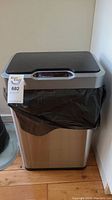 Front view of stainless steel sensor waste bin with black lid and black garbage bag fitted. Shows the overall appearance of the bin.