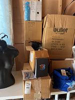 Stacked boxes containing stainless steel water bottles, assorted pens and promotional swag near a mannequin torso, indicating items included in the lot.
