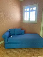 Side view of blue chaise lounge showing overall shape, blue fabric upholstery and a rolled arm on one side alongside two pillows.