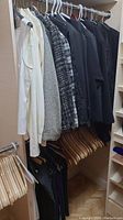 Clothing hung on hangers on rack, various sweaters, shirts, coats, and pants.