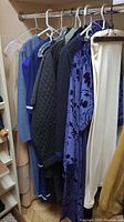 View of various women's clothing items hanging on rack including dresses, sweaters, coat, and night gowns in predominantly dark and neutral colors.