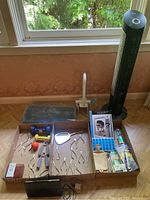 Entire assortment of items including black tower fan, dental tools in box, pill organizer, toiletry items, alarm clock, and towel displayed on wood floor.