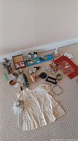 Photo showing assorted items on carpet including a child's dress, native carving, small game pieces, miniature houses, and decorative baskets