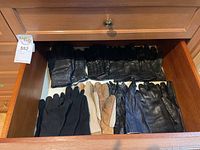 Eight pairs of gloves displayed inside a drawer, mostly leather with some knit, showing wear on leather surfaces