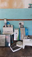 Overview of assorted health and bath aid items including scale, bath chair, seat riser, boxed handheld shower head, and boxed grab bar
