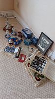 Full lot displayed on carpet showing various items including geological collection box, framed art, troll dolls, candle holders, menorah, and small pottery.
