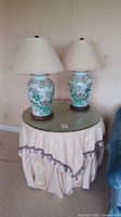 Both porcelain urn lamps on round table with draped skirt