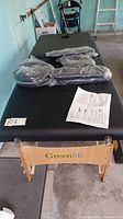 Full top view of Greenlife branded massage table with unopened accessories in plastic on the surface and instruction manual placed on the table.