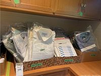 Overview of two cardboard trays filled with individually bagged shirts showing multiple brands and colors