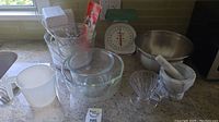 Photo of kitchen counter with electric mixer, glass mixing bowls, kitchen scale, measuring jug, glass funnel, and marble mortar and pestle.