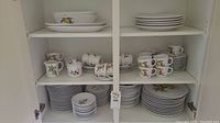 Cabinet shelf view of stacked dinner plates, salad plates, cups and mugs