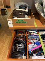 Overview of folded shirts, cap on top, belts and scarves in drawers