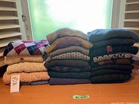 Stack of 17 assorted medium size sweaters in various colors and knitting patterns on a wooden table.